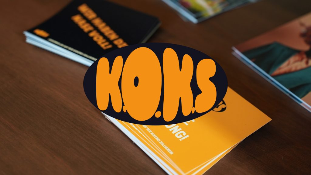 Orangefarbene Flyer mit dem Schriftzug K.O.K.S. auf einem Holztisch