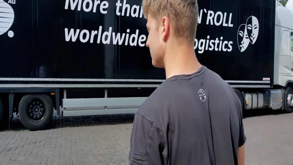 Person in grauem Shirt steht vor einem LKW mit Logistik-Aufschrift bei der Anlieferung zum Ninja Tournament