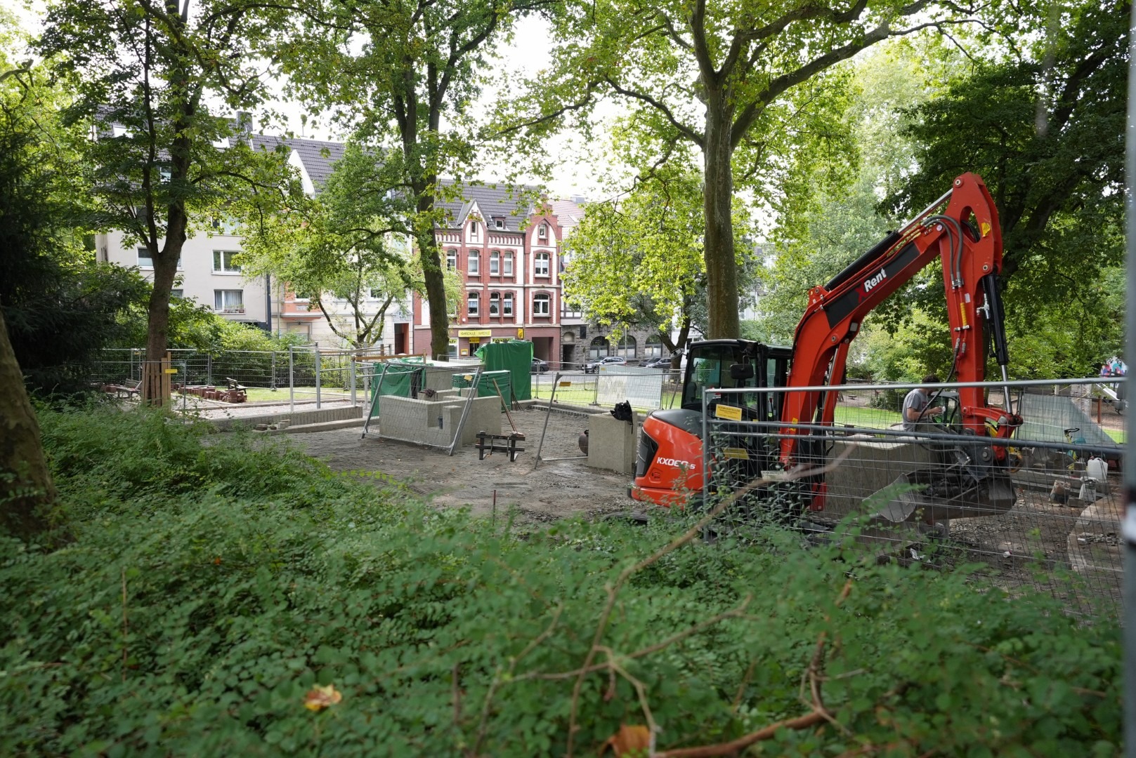 Bagger und Baumaschinen auf der eingezäunten Baustelle der Parkouranlage im Benderpark, umgeben von Bäumen
